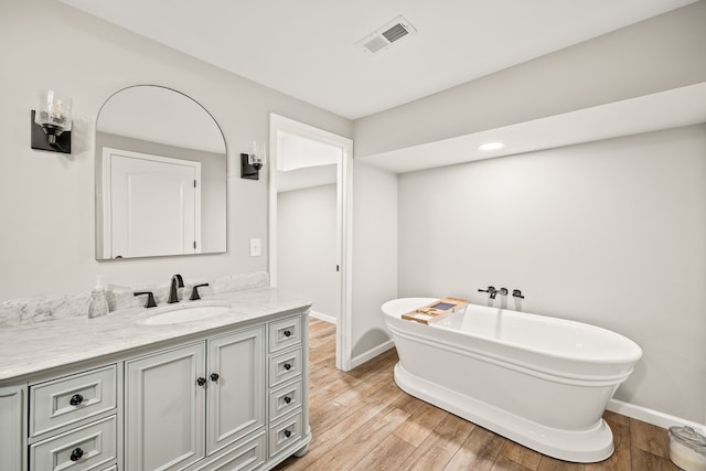 full bath with a freestanding tub, wood finished floors, vanity, visible vents, and baseboards