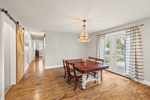 dining space featuring a barn door, wood finished floors, visible vents, baseboards, and french doors