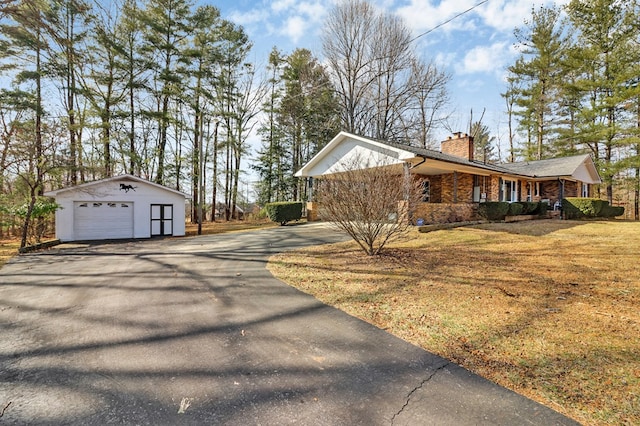 view of side of property featuring a lawn, a chimney, a detached garage, aphalt driveway, and an outdoor structure