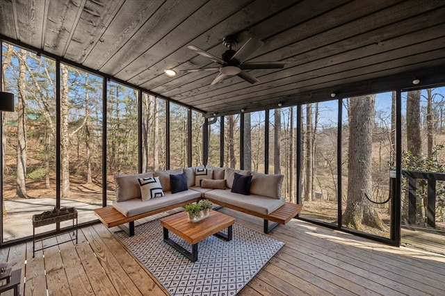 unfurnished sunroom featuring wood ceiling, a wooded view, and a ceiling fan