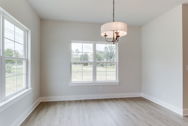 empty room with a chandelier, light wood finished floors, and baseboards