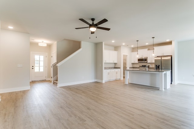 unfurnished living room featuring recessed lighting, baseboards, light wood finished floors, and stairs