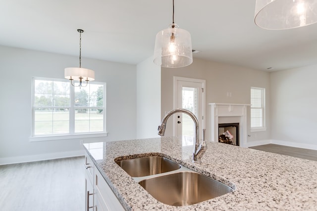 kitchen featuring decorative light fixtures, light stone countertops, white cabinets, a sink, and wood finished floors