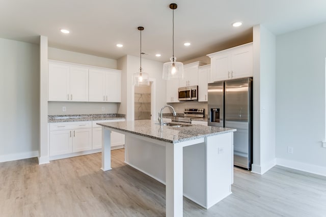 kitchen with stainless steel appliances, a center island with sink, and white cabinetry