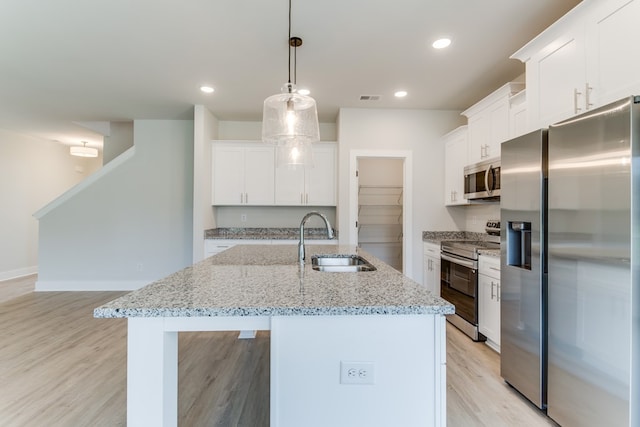 kitchen with stainless steel appliances, a sink, white cabinets, an island with sink, and decorative light fixtures