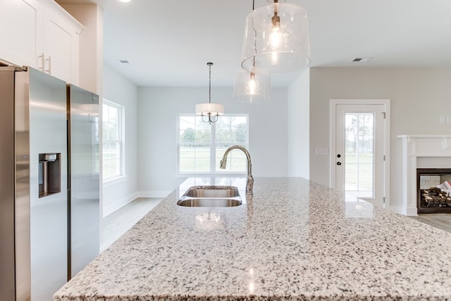 kitchen featuring a center island with sink, decorative light fixtures, white cabinetry, stainless steel refrigerator with ice dispenser, and a sink