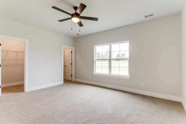 unfurnished bedroom featuring light carpet, a ceiling fan, visible vents, baseboards, and a spacious closet