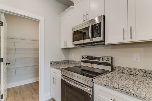 kitchen featuring stainless steel appliances, white cabinetry, baseboards, light wood-type flooring, and light stone countertops