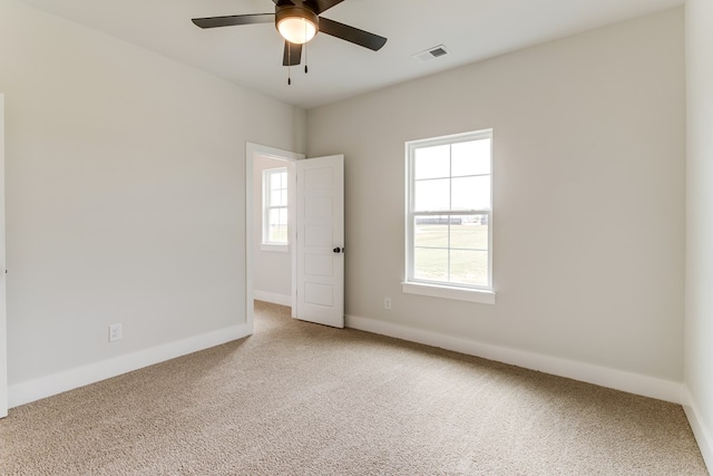 empty room with visible vents, carpet floors, a wealth of natural light, and baseboards