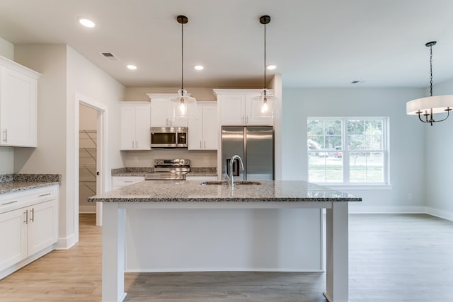 kitchen featuring an island with sink, appliances with stainless steel finishes, pendant lighting, and a sink