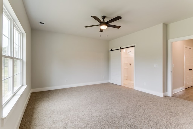 unfurnished bedroom with light carpet, visible vents, baseboards, and a barn door