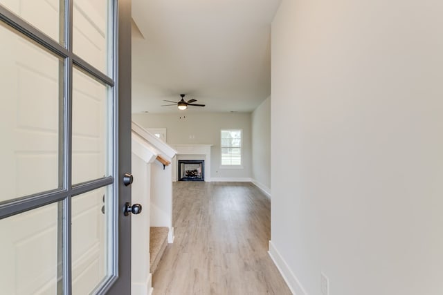 interior space featuring light wood-type flooring, ceiling fan, a fireplace, and baseboards