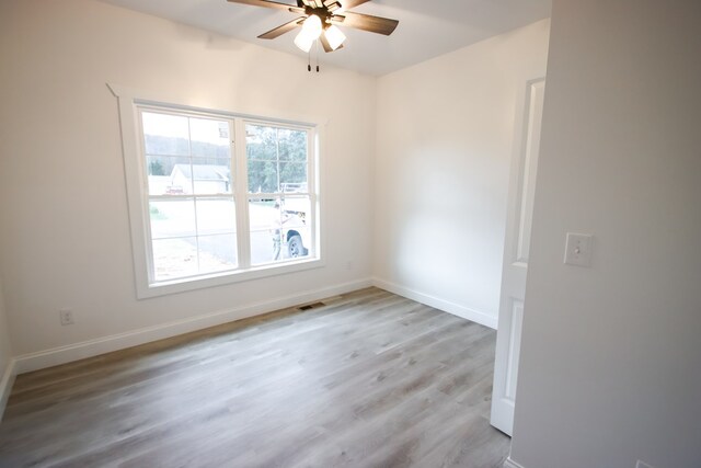 empty room featuring a ceiling fan, baseboards, visible vents, and light wood finished floors