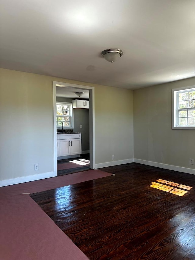 spare room featuring dark wood-type flooring, a sink, and baseboards