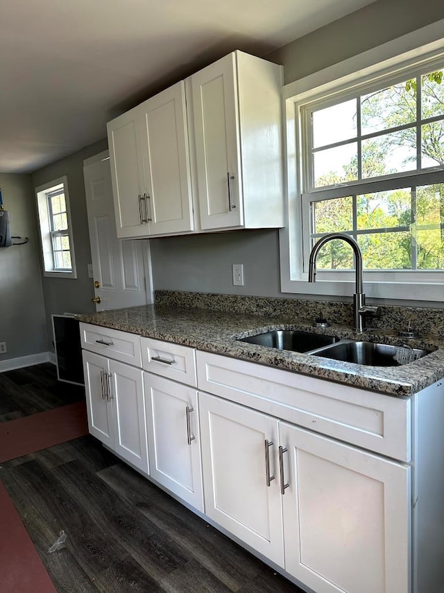 kitchen with dark wood-style flooring, a sink, white cabinetry, baseboards, and dark stone countertops