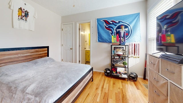 bedroom with a textured ceiling, connected bathroom, light wood-style flooring, and baseboards