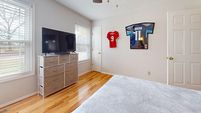 bedroom featuring light wood-type flooring, visible vents, a textured ceiling, and baseboards