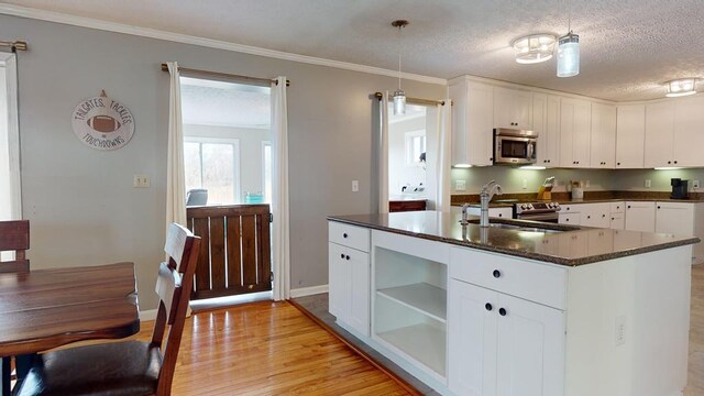 kitchen featuring light wood-style flooring, white cabinets, open shelves, stainless steel microwave, and dark stone countertops