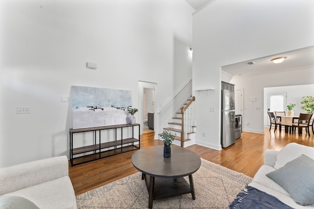 living area with light wood finished floors, visible vents, baseboards, stairway, and ornamental molding