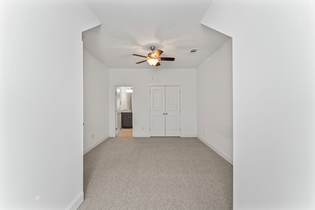 empty room featuring a ceiling fan, light colored carpet, visible vents, and baseboards