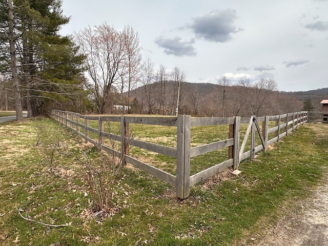 view of yard featuring a rural view, a wooded view, and fence