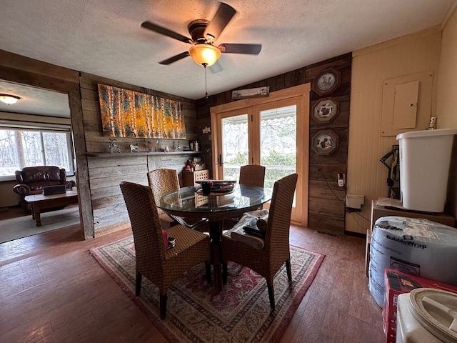 dining area featuring a ceiling fan, wood walls, wood-type flooring, and a textured ceiling