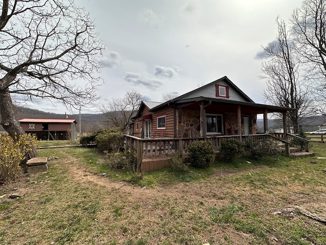 view of side of home featuring stone siding, a lawn, and covered porch