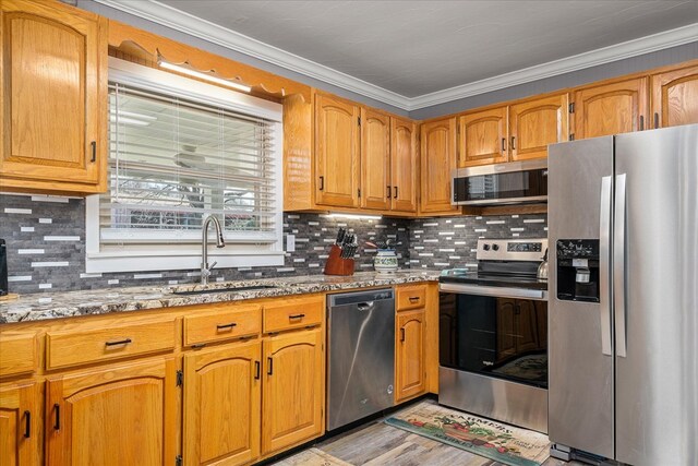 kitchen with light stone counters, stainless steel appliances, a sink, light wood-type flooring, and crown molding