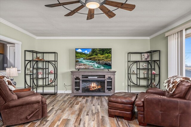 living area featuring a lit fireplace, ornamental molding, wood finished floors, and a ceiling fan