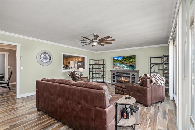 living room featuring light wood-style floors, baseboards, crown molding, and a glass covered fireplace