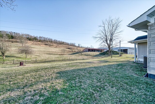 view of yard with fence, central AC, and a rural view