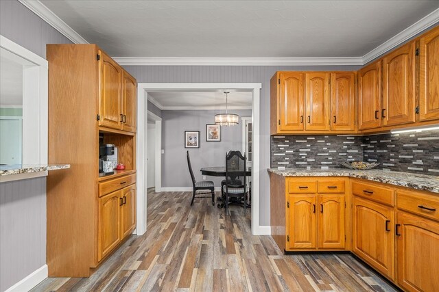 kitchen featuring light stone counters, dark wood-style floors, tasteful backsplash, hanging light fixtures, and ornamental molding