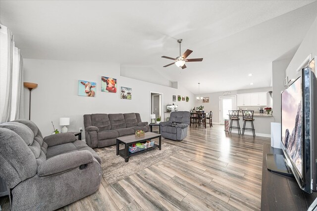 living room with lofted ceiling, light wood-style flooring, baseboards, and a ceiling fan