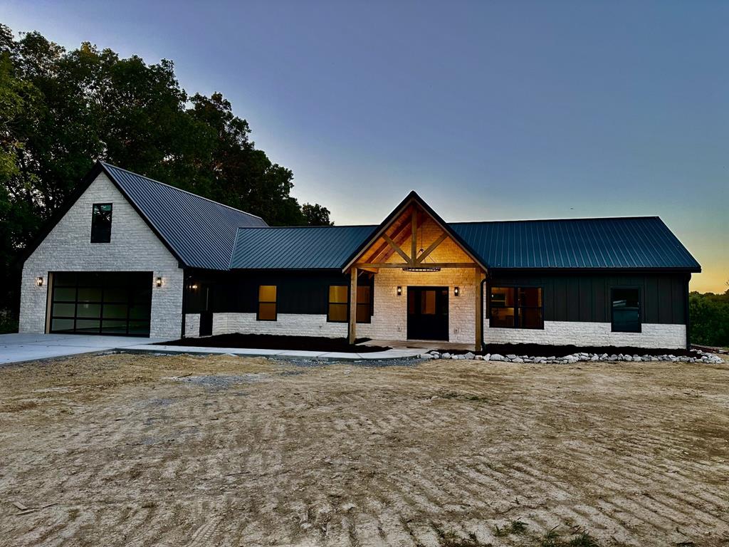 modern farmhouse with board and batten siding, brick siding, metal roof, and driveway