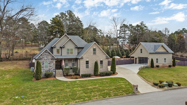 craftsman house featuring stone siding, a detached garage, fence, and a front yard