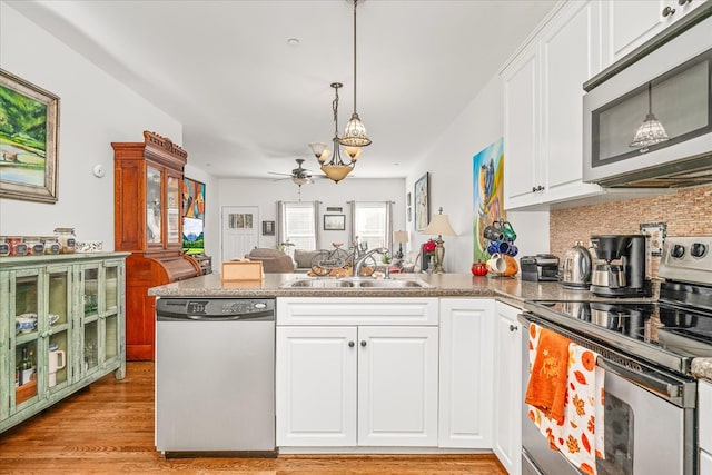 kitchen featuring hanging light fixtures, appliances with stainless steel finishes, open floor plan, white cabinets, and a sink