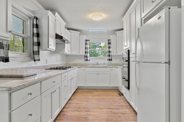 kitchen with light stone counters, a sink, white cabinets, appliances with stainless steel finishes, and light wood finished floors