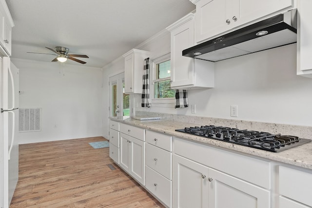 kitchen with black gas stovetop, under cabinet range hood, white cabinetry, ornamental molding, and freestanding refrigerator