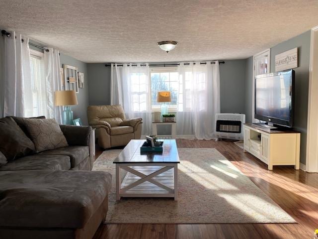 living area with a textured ceiling, heating unit, and wood finished floors