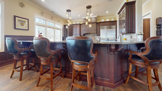 bar with ornamental molding, backsplash, stainless steel built in fridge, dark wood finished floors, and decorative light fixtures