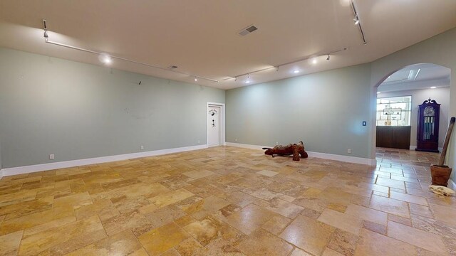 spare room with arched walkways, stone tile floors, visible vents, baseboards, and track lighting