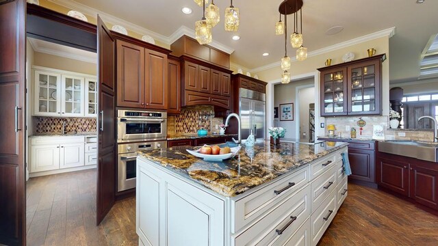 kitchen featuring a center island with sink, glass insert cabinets, decorative light fixtures, stainless steel appliances, and white cabinetry