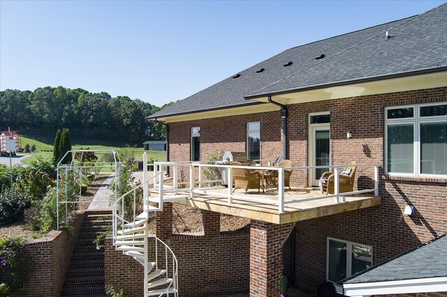 rear view of house featuring a shingled roof, brick siding, and stairway