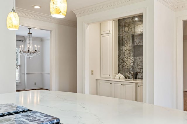 kitchen with light stone counters, recessed lighting, hanging light fixtures, ornamental molding, and a sink