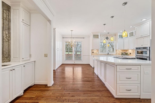 kitchen featuring white cabinets, glass insert cabinets, light countertops, pendant lighting, and a sink