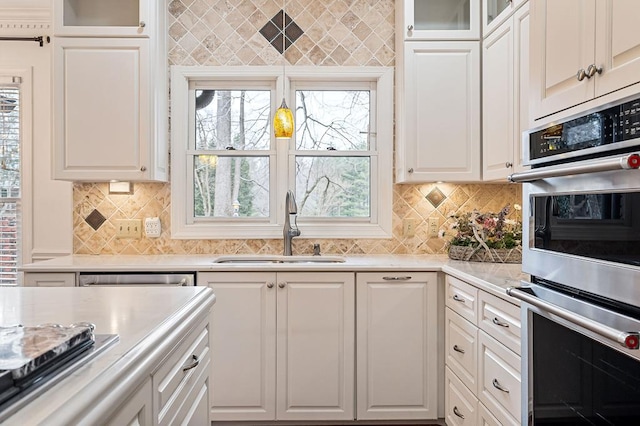 kitchen featuring a sink, white cabinets, appliances with stainless steel finishes, tasteful backsplash, and glass insert cabinets