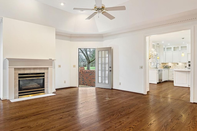 unfurnished living room featuring a raised ceiling, dark wood-type flooring, ceiling fan, a tile fireplace, and baseboards