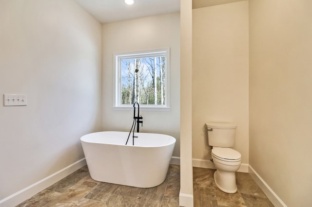 bathroom with a soaking tub, baseboards, and toilet