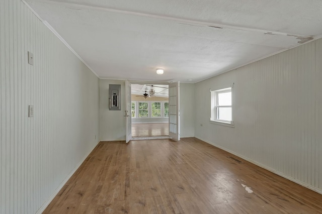 unfurnished room featuring wood finished floors, visible vents, baseboards, ornamental molding, and electric panel