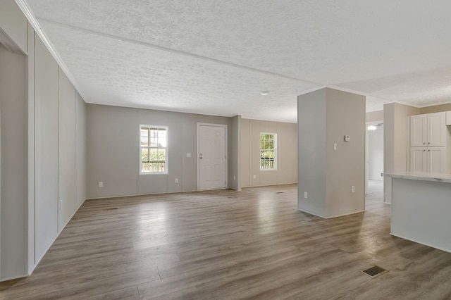 spare room with a textured ceiling, ornamental molding, wood finished floors, and visible vents